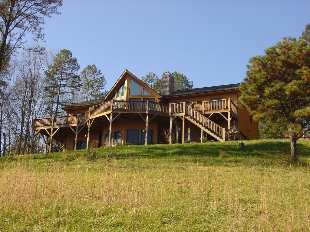 Yellow-orange hillside home with multi-level wood deck, stone chimney, and gable windows